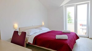 A hotel room with a bed, a desk, and a chair. There is a window with a view of the outside. - Apartment Sucic Tea 4 (Soline - island Krk)