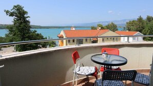 A balcony with a table and chairs, overlooking a body of water and buildings. - Apartment Sucic Tea 4 (Soline - island Krk)