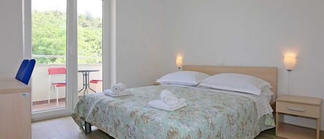 A bedroom with a bed, two bedside tables, a window, and a balcony with chairs.