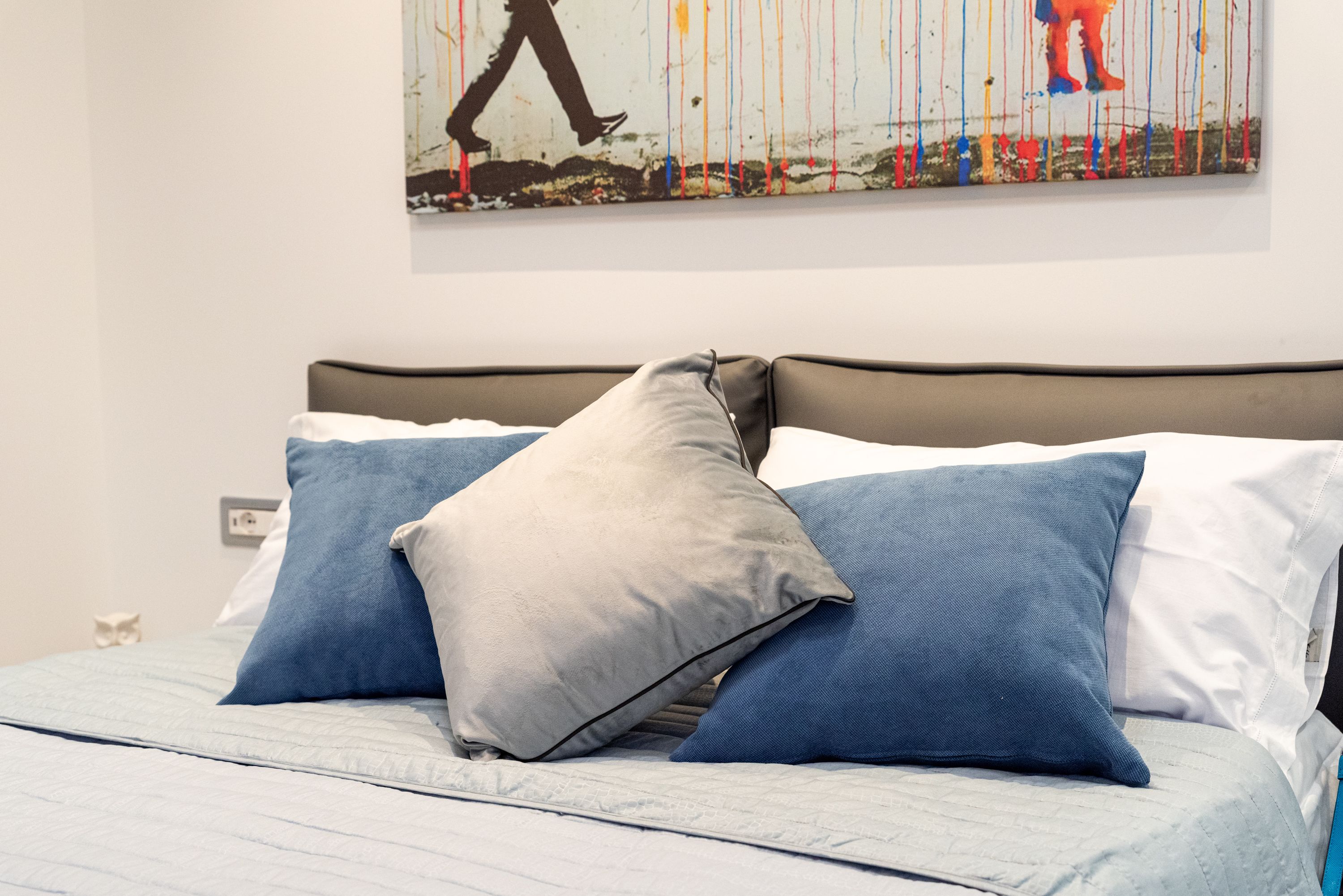 Un lit bien fait, agrémenté d’un arrangement d’oreillers aux tons de gris et de bleu.