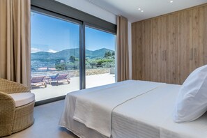 Ein Schlafzimmer mit großem Fenster, einem Bett und einem Korbstuhl.