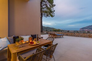 Ein Holztisch mit Speisen und Getränken, mit Blick auf eine malerische Küstenlandschaft und Liegestühle.