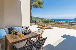 Eine Terrasse mit Frühstückstisch, Liegestühlen und einem schönen Meerblick.