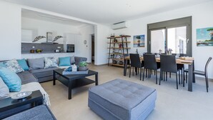 Ein modernes Wohnzimmer mit einer Couch, Hocker und einem Essbereich mit Stühlen und einem Tisch.