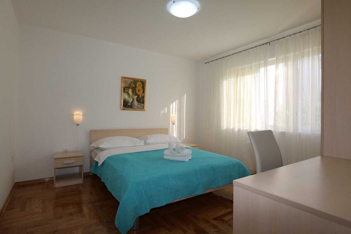 Hotellihuone, jossa on sänky, yöpöytä, työpöytä, tuoli, seinällä taulu ja ikkuna, jossa on verhot.