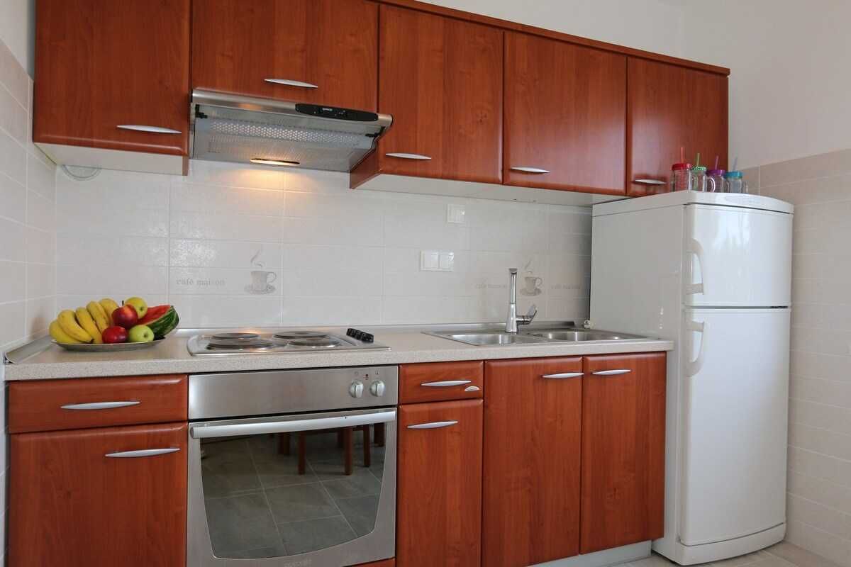 Eine Küche mit Holzausstattung, einem Edelstahlbackofen, einem weißen Kühlschrank und einer Obstschale auf der Arbeitsfläche.