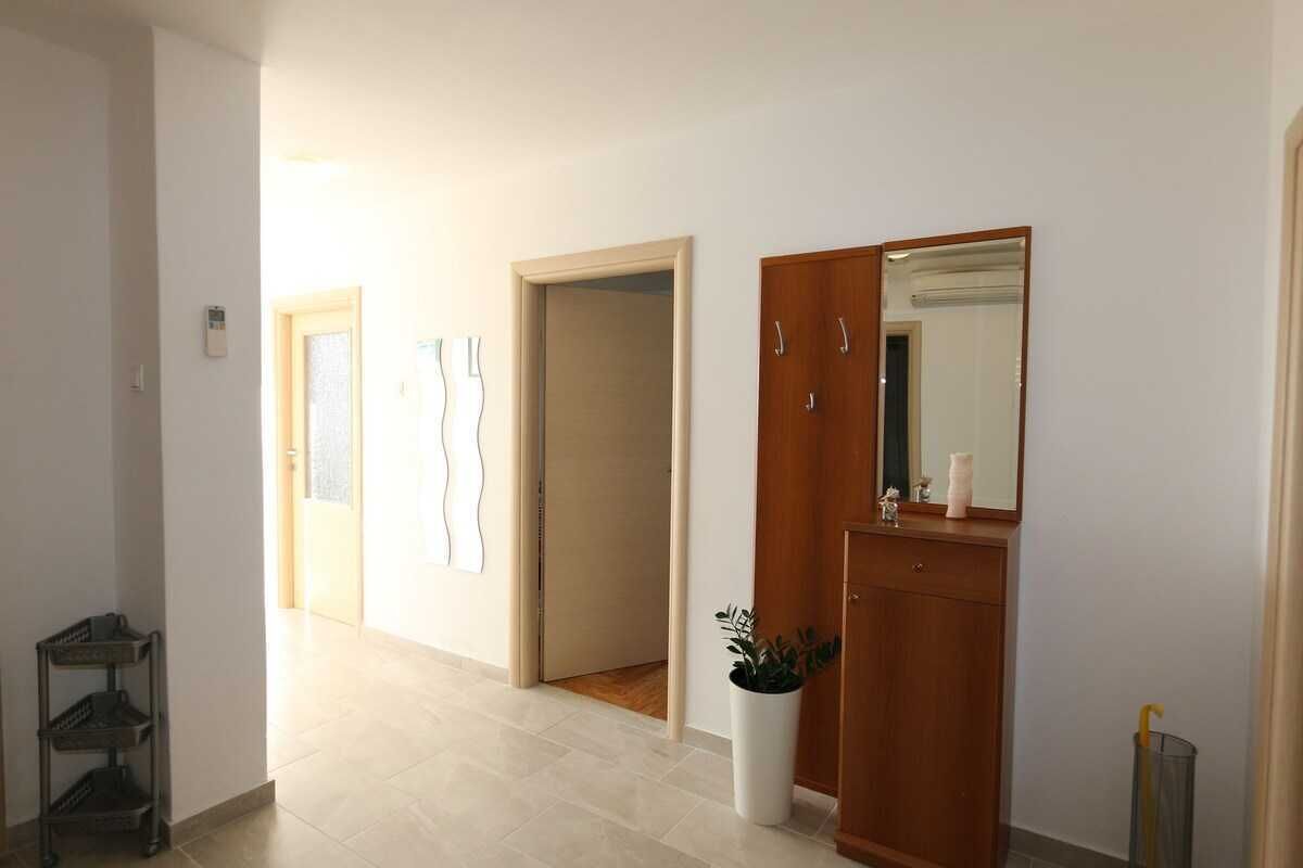 En hall med en garderob i trä, en krukväxt och ett metallställ.