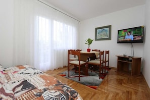 Una habitación con cama, una mesa de comedor con sillas, un televisor y una planta pequeña.