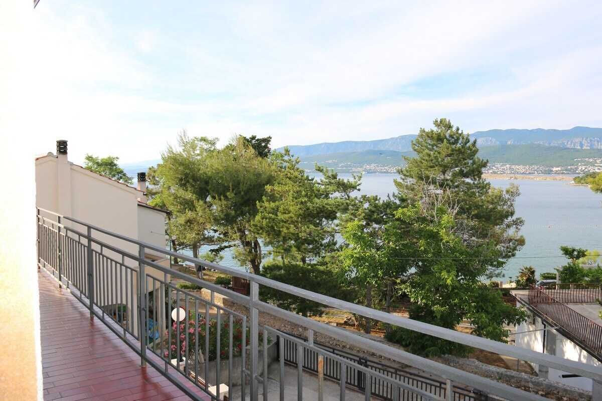 A balcony with a railing overlooking a body of water, trees, and distant hills.