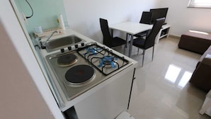 Cozinha compacta com fogão a gás, pia e área de refeições com cadeiras e mesa.