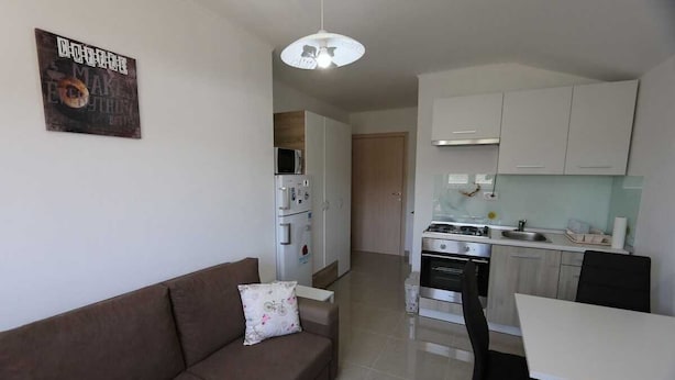 Uma sala de estar moderna com sofá, mesa de jantar e área de cozinha com armários e eletrodomésticos.