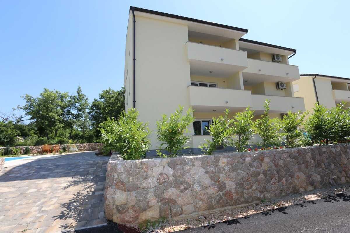 Un edificio a più piani con balconi, un muro di sostegno in pietra e un'area pavimentata.