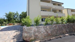 Um edifício com vários andares, varandas, um muro de pedra e um espaço pavimentado.