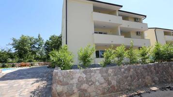 Un edificio a più piani con balconi, un muro di sostegno in pietra e un'area pavimentata.