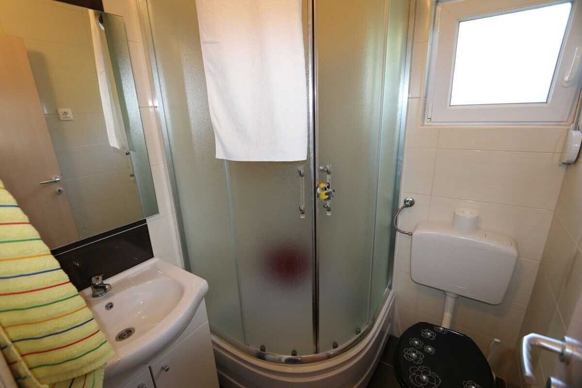 Ein Badezimmer mit einer Duschkabine, einem Waschbecken, einer Toilette und einem Fenster.