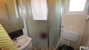 Ein Badezimmer mit einer Duschkabine, einem Waschbecken, einer Toilette und einem Fenster.