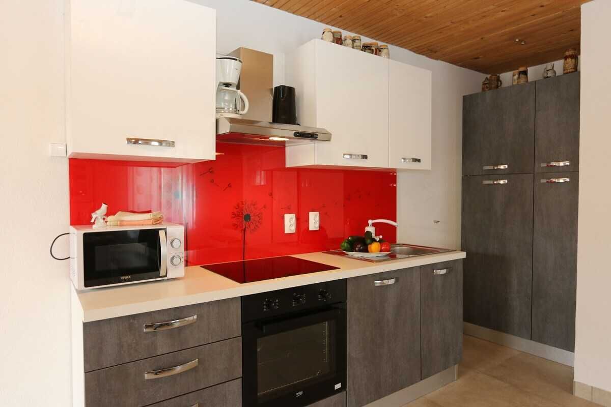 A modern kitchen with a red backsplash, a microwave, a stove, and cabinets.