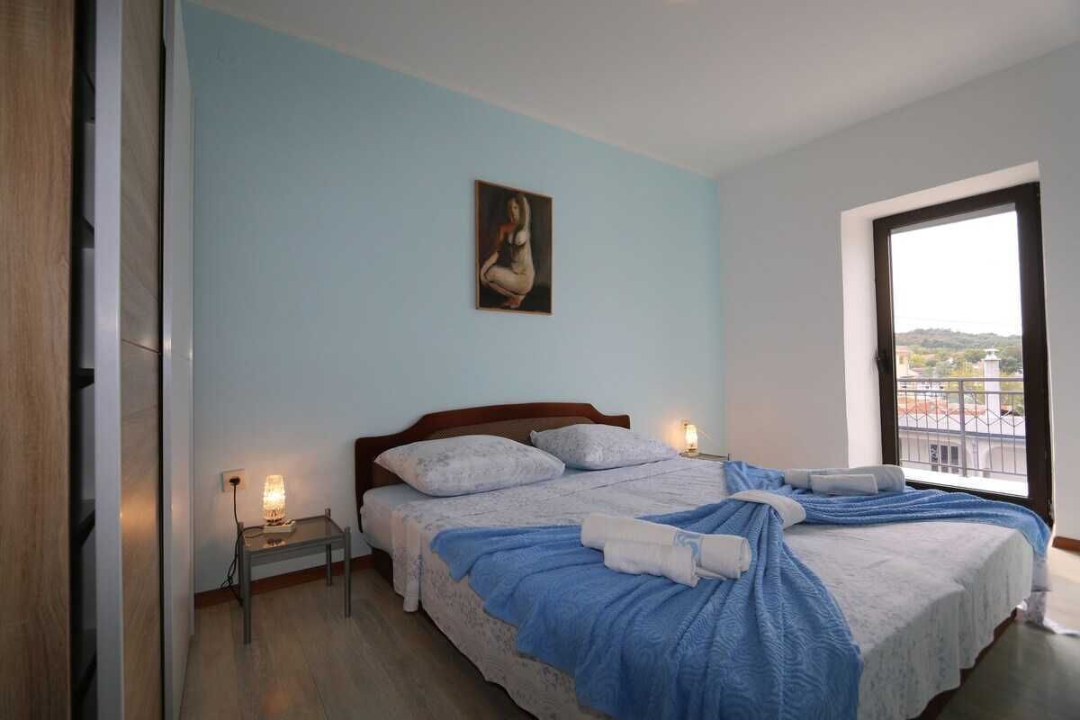 A bedroom with a bed, bedside lamps, a painting, and a window with a view.