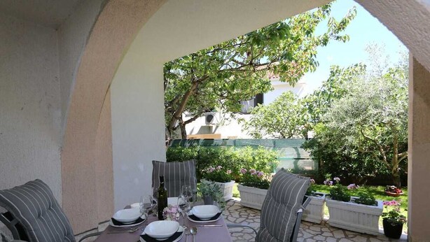 An outdoor dining area with a table set for two, surrounded by stone flooring and potted plants. - Apartment Brusic dole (Silo - island Krk)