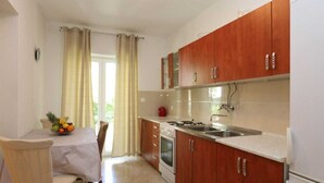 A kitchen with wooden cabinets, a stainless steel sink, and a dining table with a fruit bowl. - Apartment Brusic dole (Silo - island Krk)