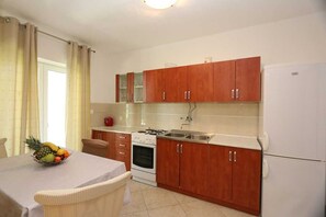 A kitchen with wooden cabinets, a stove, a sink, and a refrigerator. - Apartment Brusic dole (Silo - island Krk)