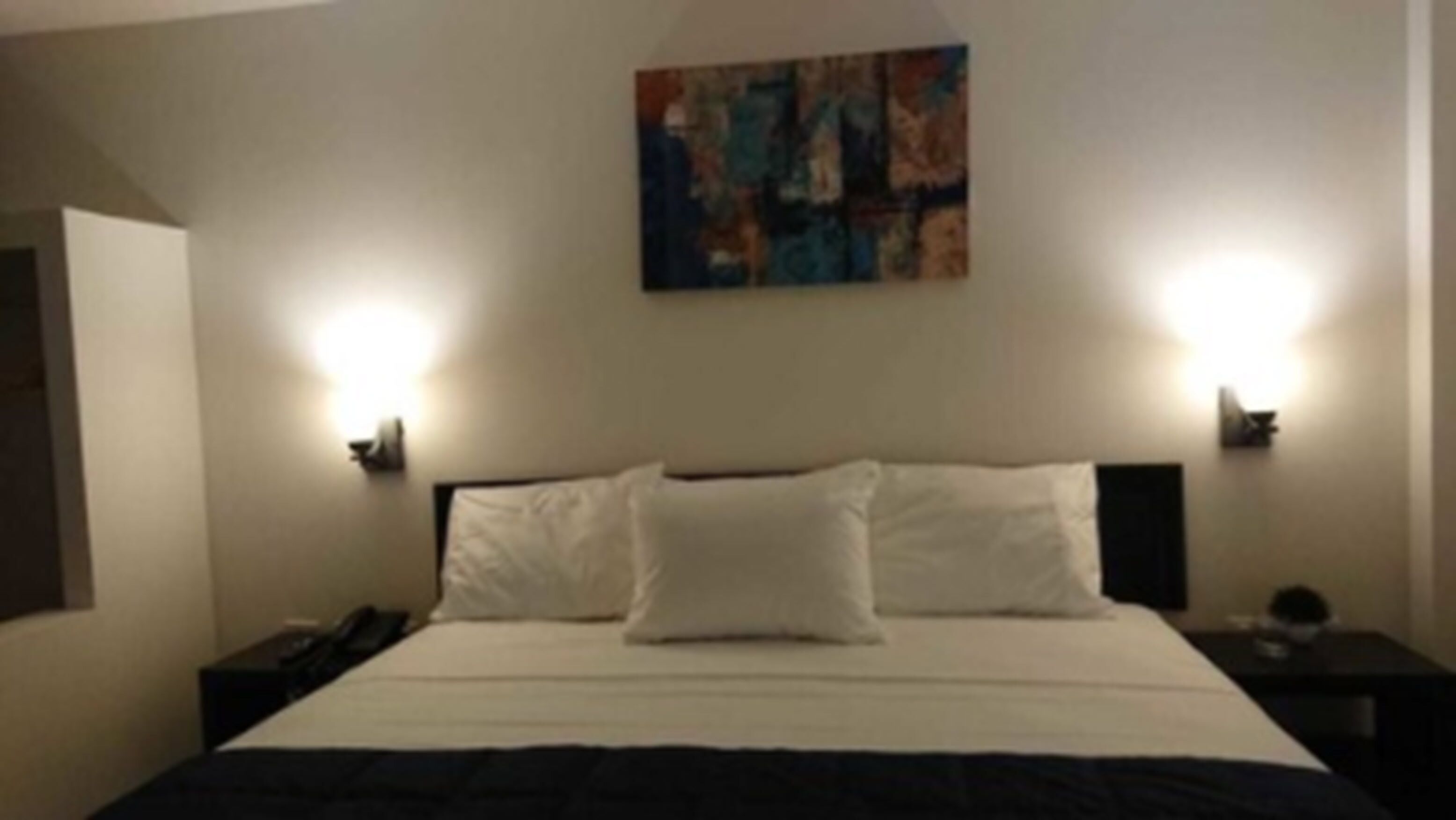 Un cuarto de hotel con una cama grande, dos lámparas de noche y un cuadro en la pared.