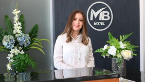 Un comptoir d’accueil orné du logo de l’hôtel MB, deux compositions florales et un mur noir.