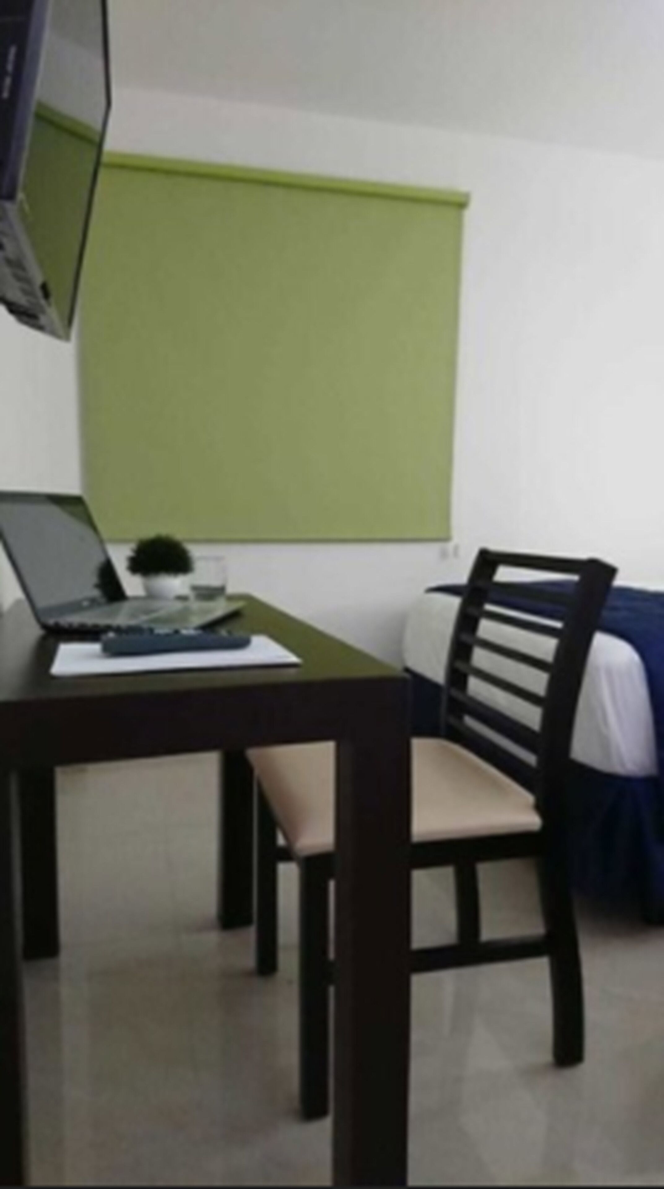 Une petite pièce avec un bureau, une chaise, un lit et un mur vert.