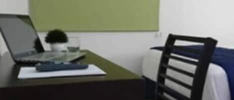 A small room with a desk, a chair, a bed, and a green wall.