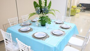Une table à manger dressée pour six personnes, avec des chaises blanches, une nappe bleue et un centre de table floral.