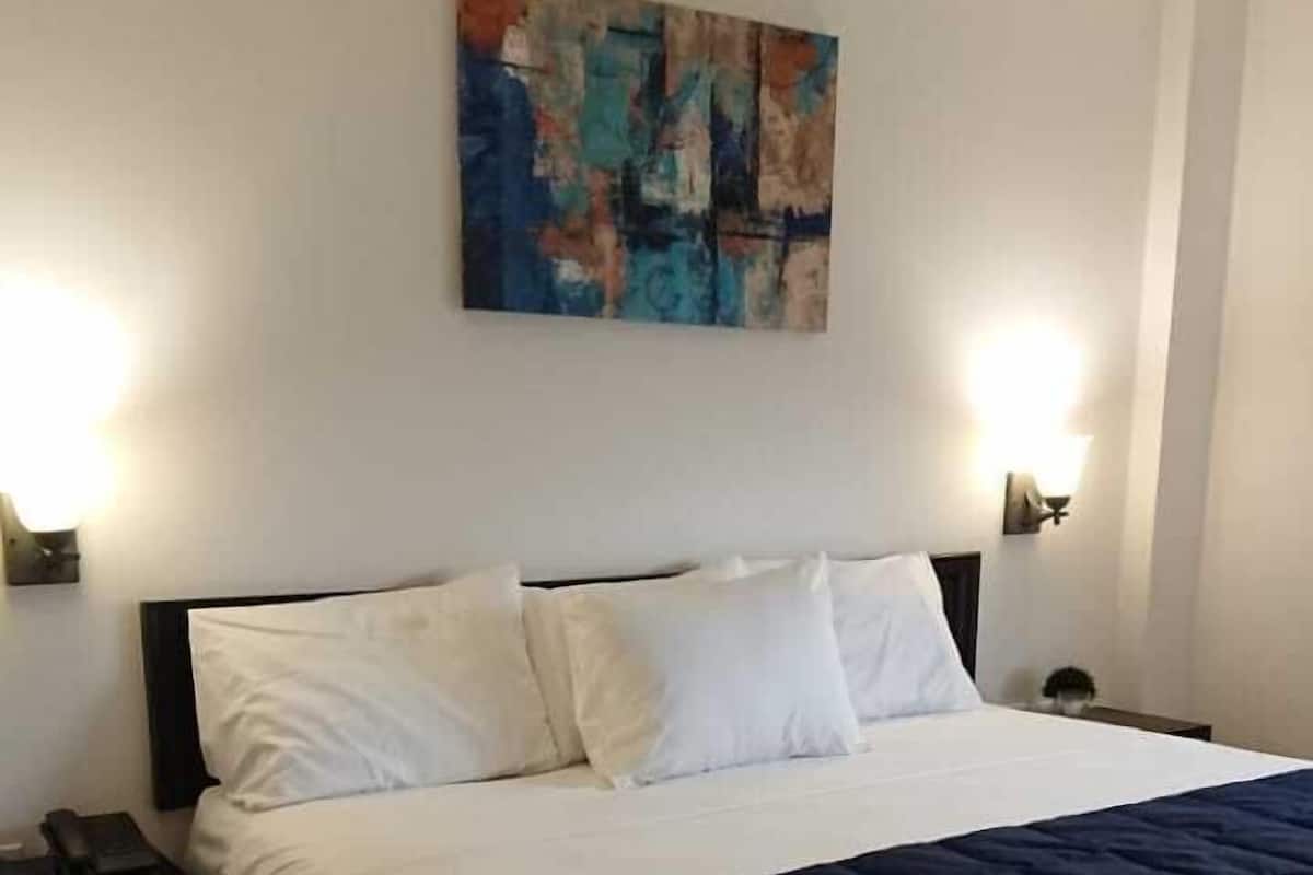 Ein ordentlich bezogenes Bett mit weißer und marineblauer Bettwäsche, ein moderner Kopfteil und ein einzelnes abstraktes Gemälde an der Wand.