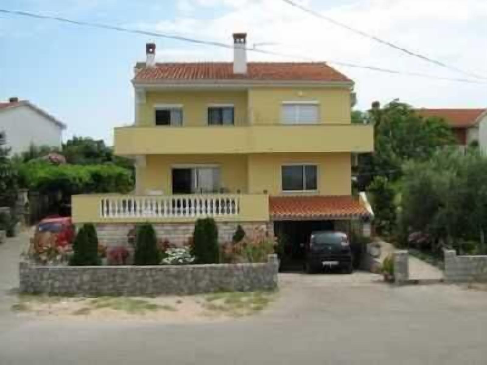 A two-story yellow building with a white fence, a garage, and a driveway.