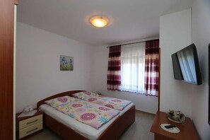 Quarto com uma cama, mesa de cabeceira, televisão e janela com cortinas.
