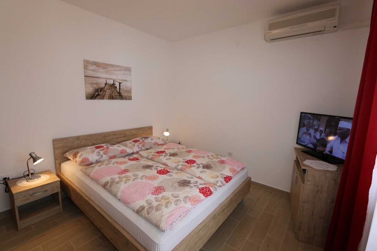 Ein Schlafzimmer mit einem Bett, einem Nachttisch mit Lampe, einem Fernseher und einem Bild an der Wand.