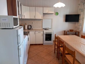 Een compacte keuken met witte apparaten, een eethoek met tafel en stoelen, en een flatscreen tv aan de muur.