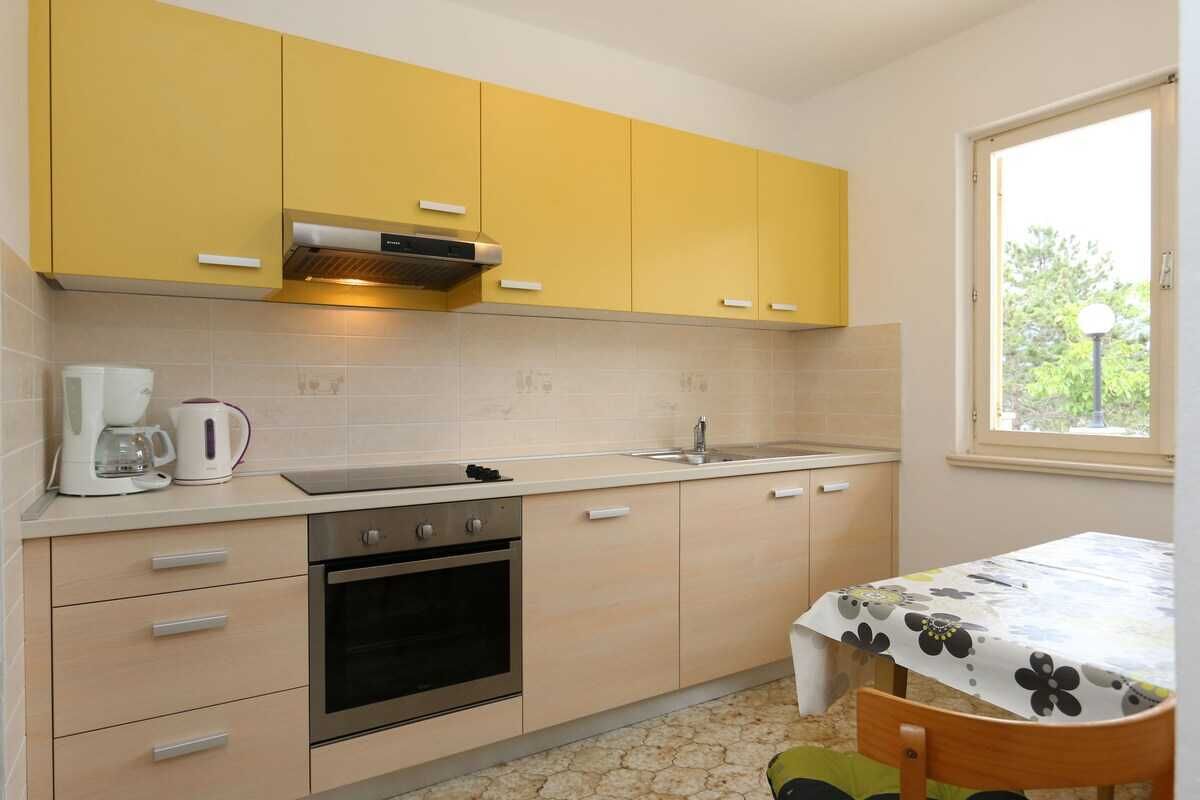 Une cuisine compacte avec des meubles de couleur jaune, un four encastré, un évier et une fenêtre qui laisse entrer la lumière naturelle.