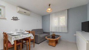 A dining area with a table set for four, a grey sofa, a small wooden side table with a vase, and a television on a cabinet.