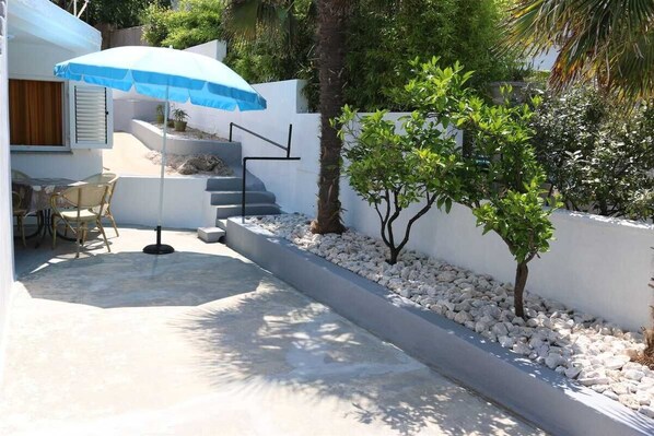 Eine Terrasse mit Tisch und Stühlen, einem blauen Sonnenschirm, einer Treppe und einem kleinen Baum.