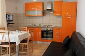 Une cuisine compacte avec des meubles de rangement orange, une cuisinière à gaz et un coin repas comprenant une table et des chaises.