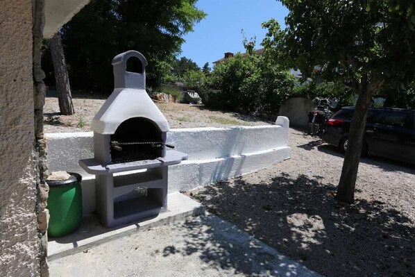 A portable outdoor oven with a chimney, a green trash bin, and a concrete barrier. - Apartment Hodzic nr 1 (Silo - island Krk)