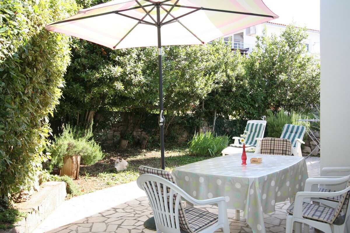 A patio with a table and chairs, surrounded by greenery and a stone pathway.