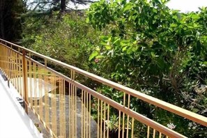 Une balustrade en bois donnant sur une végétation luxuriante et surplombant une structure en pierre.