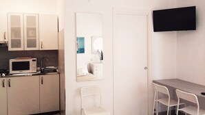 Een kleine keuken met een magnetron, kastjes en een eethoek met twee stoelen en een tafel.