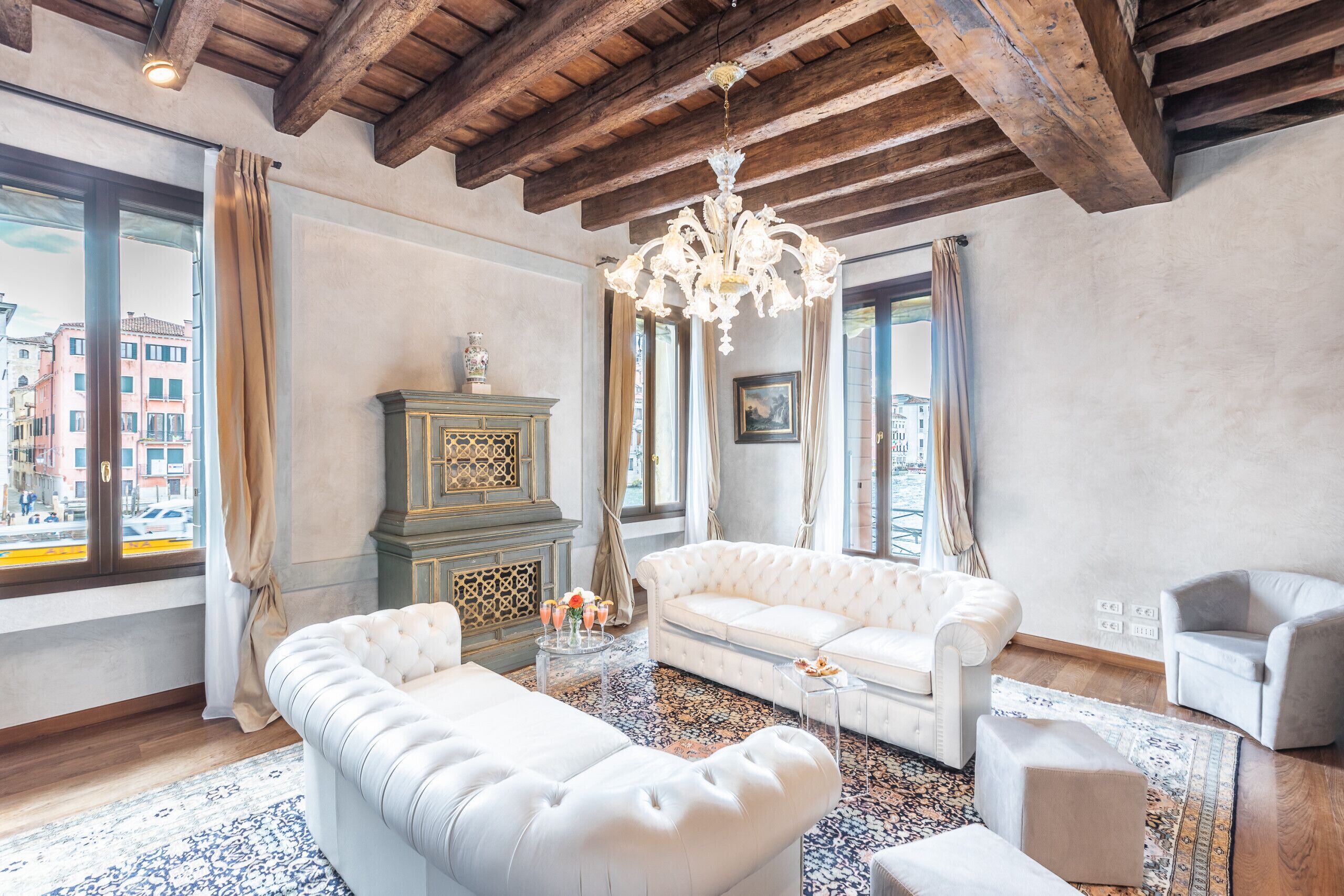 A spacious living room with a high ceiling, a chandelier, a white sofa, a beige armchair, and a patterned rug.