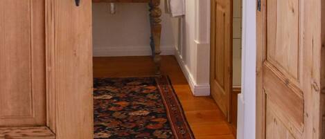 A narrow hallway with wooden doors and a mirror above a sink.