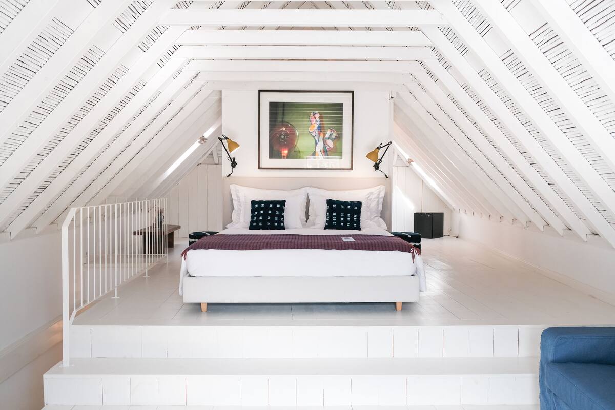 Ein modernes Schlafzimmer mit schräg versiegelter Decke, einem großen Bett und einem Rahmenbild darüber.