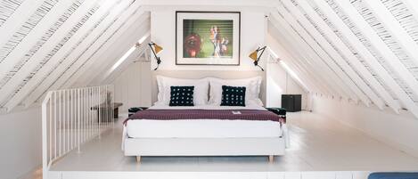 Une chambre moderne avec un plafond en pente, un grand lit et un tableau encadré au-dessus.