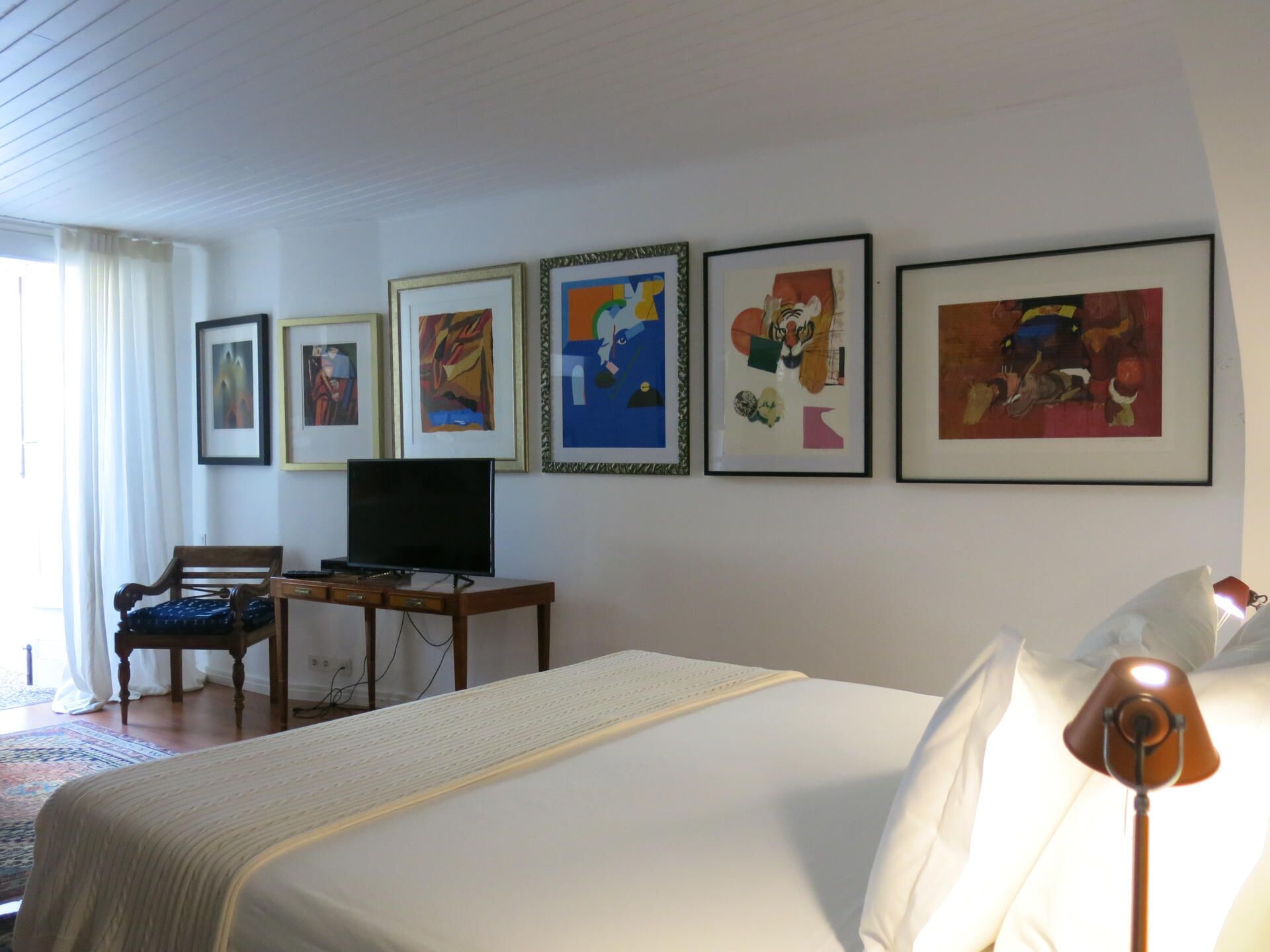 Ett hotellrum med en säng, en tv, ett skrivbord och en stol. På väggen hänger fem inramade konstverk.