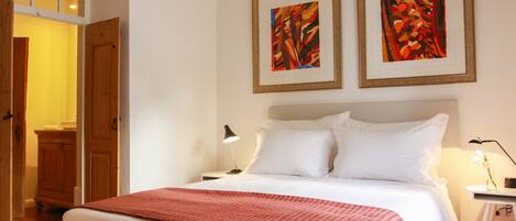 A bedroom with a large bed, a nightstand with a lamp, and two framed abstract paintings on the wall.