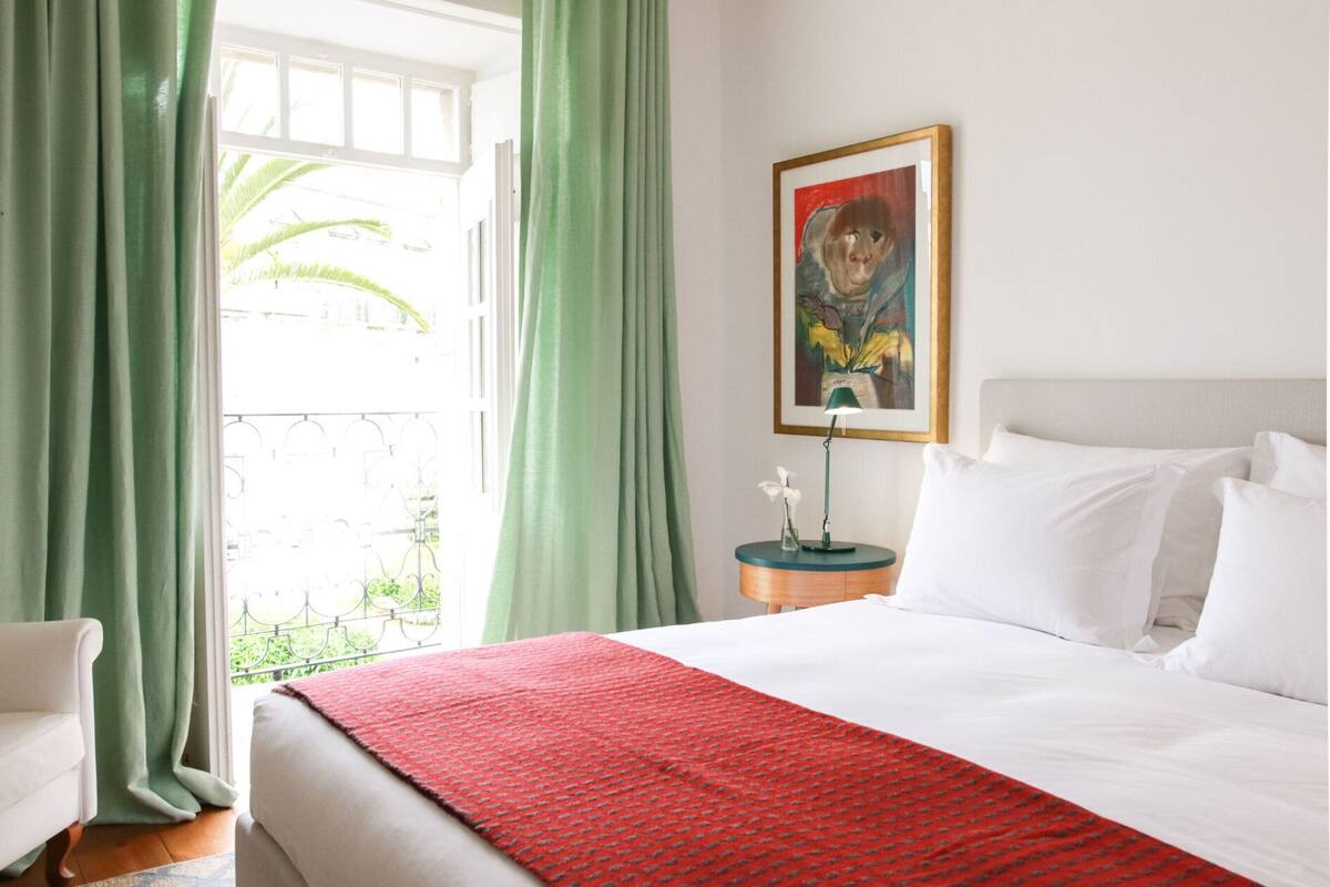 Ein Hotelzimmer mit einem Bett, einem Nachttisch, einem Gemälde und einem Fenster mit Vorhängen.